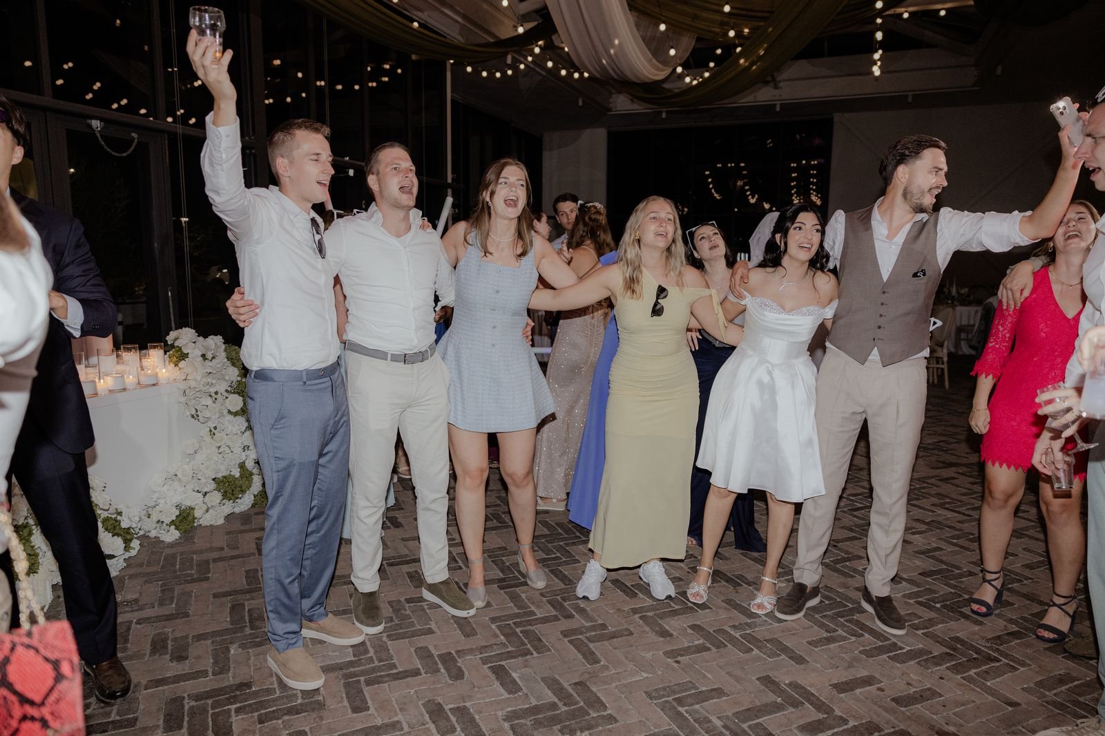 Gasten dansen met de armen omhoog op een volle dansvloer onder lichtjes