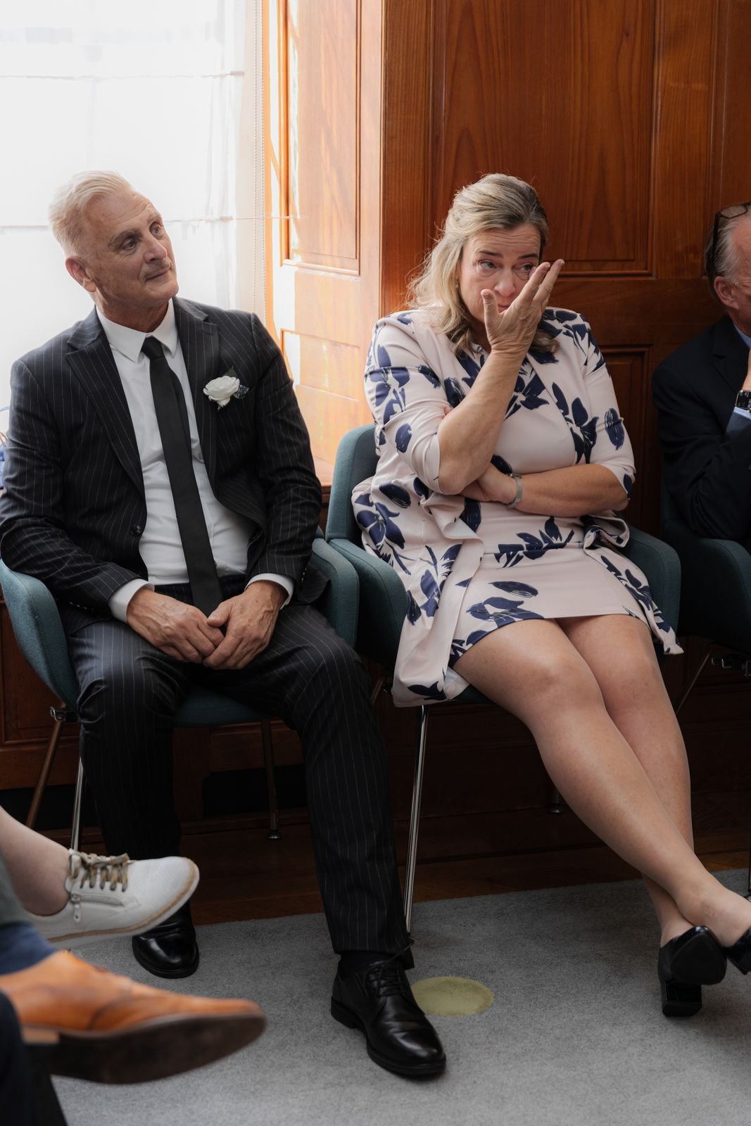 Een man en een vrouw zitten tijdens de ceremonie, de vrouw veegt een traan weg