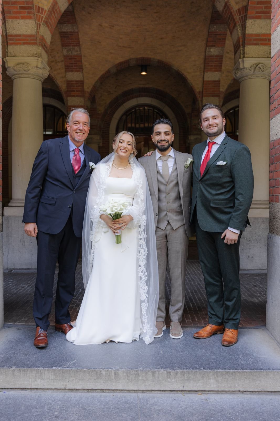 Bruid en bruidegom staan met een groep gasten in een gewelfde gang