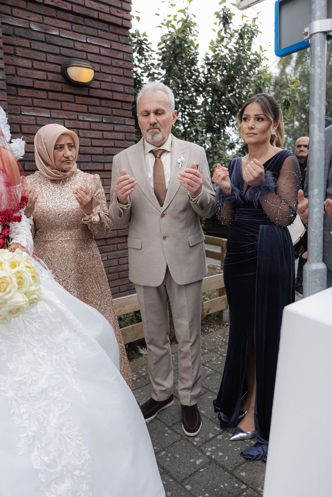 Een man en twee vrouwen staan naast elkaar en klappen terwijl de bruid voorbijloopt