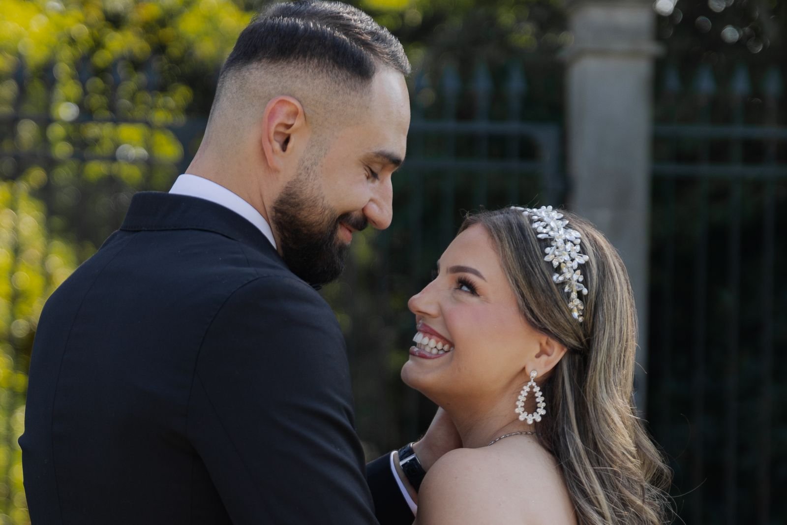 Bruidegom en bruid met tiara lachen elkaar toe in een tuin